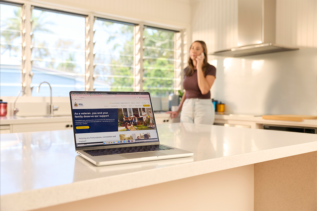 RSL Queensland website open on laptop, woman in the background on phone.