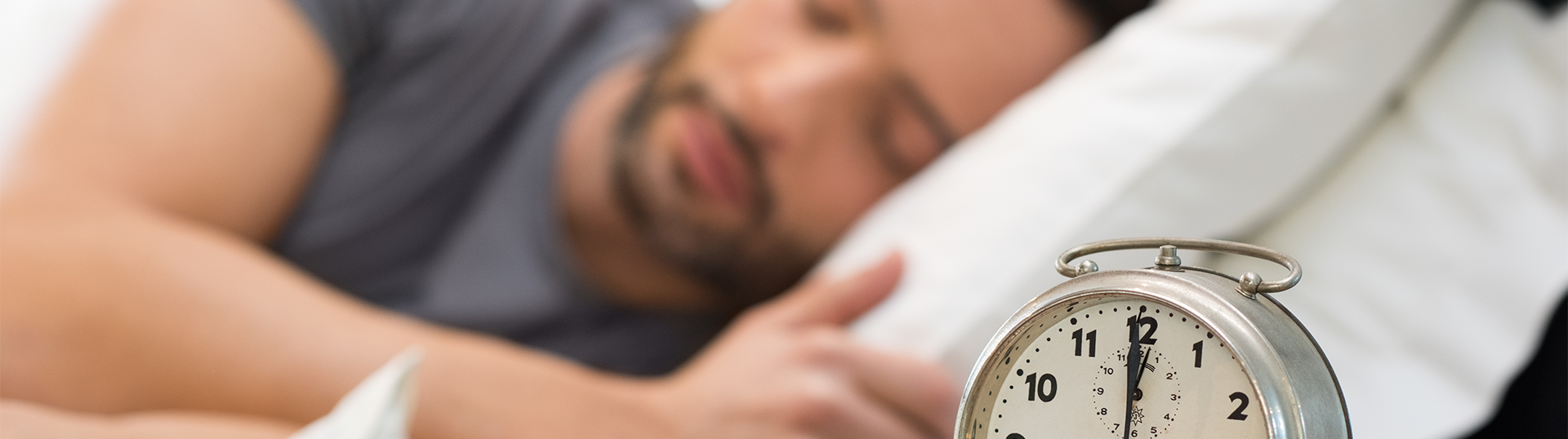 Person sleeping in bed with a clock beside